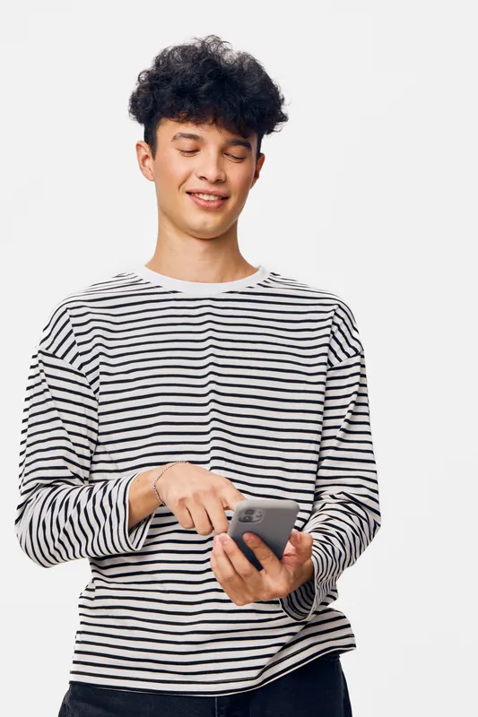 young man wearing striped shirt smiling while using smartphone, casual style, modern technology, relaxed posture, isolated white background, positive mood
