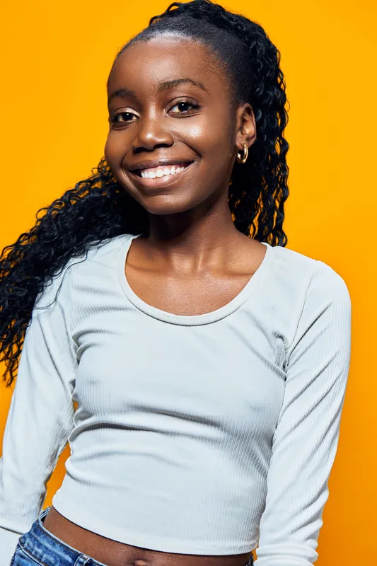Happy young African American girl with curly hair, wearing a light blue top, smiling against a vibrant yellow background, conveying joy and positivity