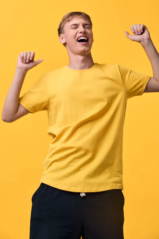 Cheerful man in a bright yellow t shirt raises arms in celebration, exuding energetic mood and victory in a studio setting with a vivid yellow backdrop and dynamic, confident pose