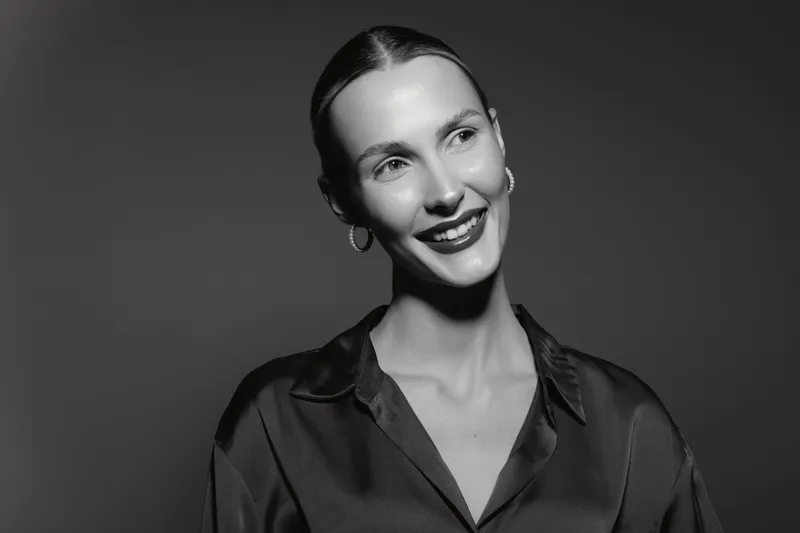 Smiling Caucasian woman with fair skin looks away in black and white photo, wearing silk blouse and hoop earrings. Concept for elegance, fashion, and beauty portrait.