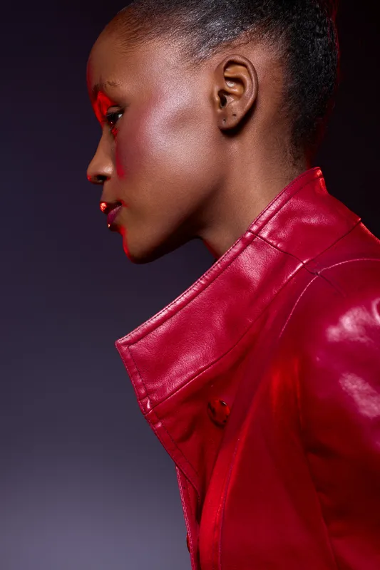 Profile of an African woman with dark skin wearing a shiny red leather jacket, photographed against a dark purple background. Concept of fashion, elegance, and beauty.
