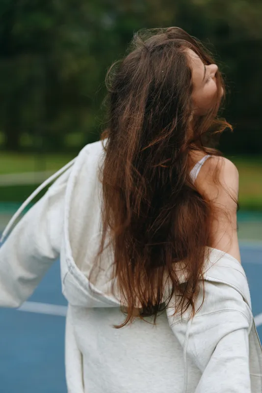 Young woman enjoying life outdoors, with long hair blowing in the wind, wearing a casual grey hoodie, embodying a carefree and relaxed summer vibe