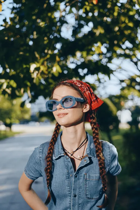 lifestyle woman in modern boho-western denim street style wearing blue sunglasses and red bandana, film color with natural outdoor background and warm sunlight