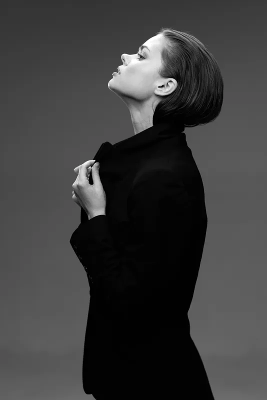 Black and white portrait of a thoughtful woman in a black jacket with a minimalist background.