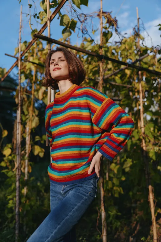 Woman striped sweater jeans outdoors portrait in sunlit garden, relaxed pose and casual fashion for autumn lifestyle, natural light and cozy knitwear mood for editorial use.