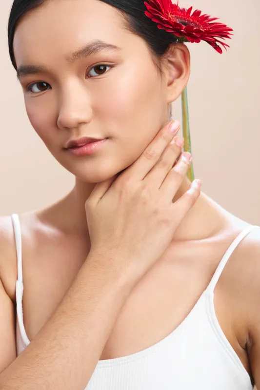 asian woman with a flower in her hair gazes softly at the camera, a serene portrait that highlights natural light, gentle beauty, and a calm, elegant mood.