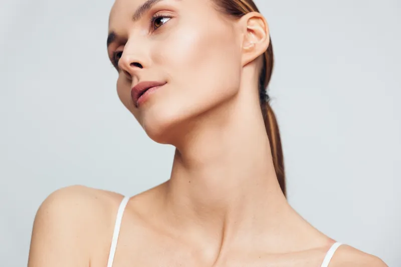 Woman portrait closeup skincare studio soft light, beauty care mood, calm expression, neutral background, natural smooth skin radiance, relaxed shoulders, white lingerie strap top