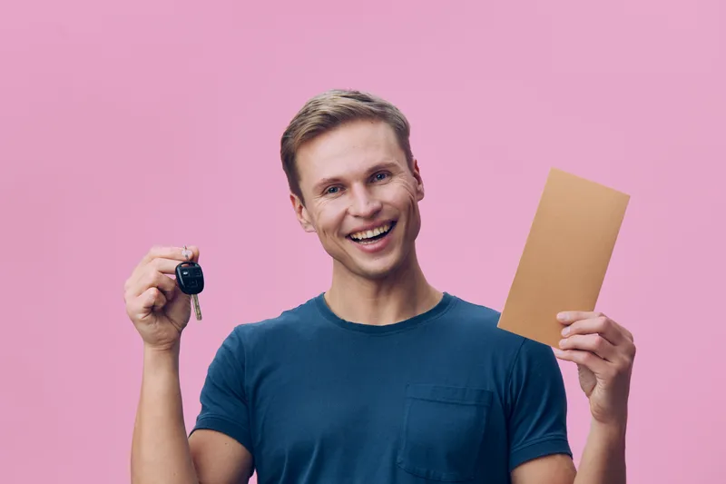 smiling young caucasian man hold car key and envelope gesture digital nomad concept on pink background