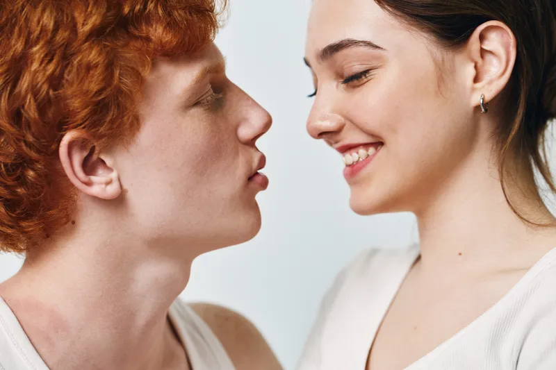 Couple, man and woman in closeup facing each other with tender expression, smiling and intimate moment indoors on white background. Young adults showing affection and connection.