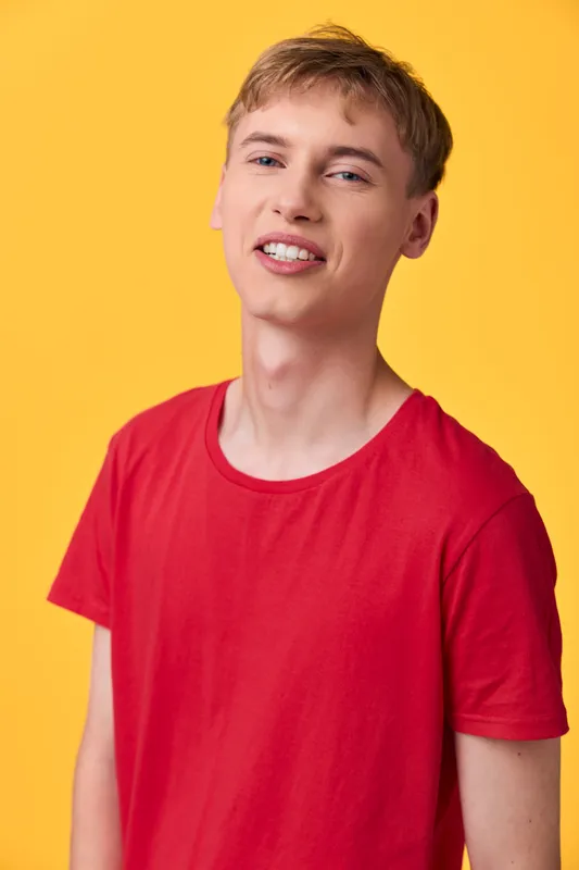 Young man in red shirt stands in a bright studio with a yellow background, showcasing a casual pose and friendly smile for lifestyle and fashion stock