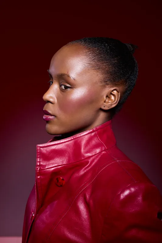 Profile of African woman with dark skin wearing a red leather jacket on red background. Studio portrait of confident black female model with natural hair in vibrant fashion concept.