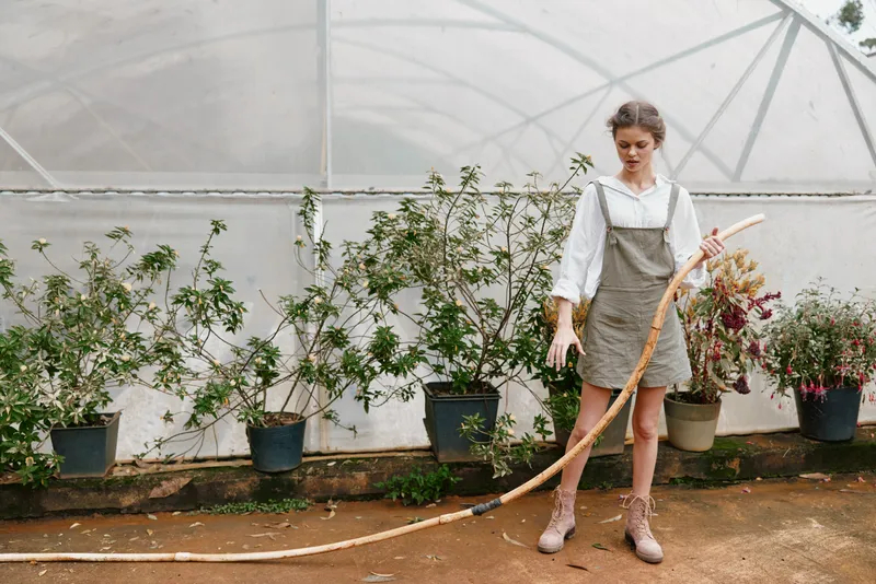 Young woman in a greenhouse, wearing a casual outfit, gardening and holding a stick, conveying a sense of connection with nature and sustainability