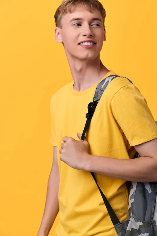 Student in a bright yellow shirt with a backpack over the shoulder, standing against a vivid backdrop. Casual fashion and learning vibe convey readiness for class, exploration, and daily adventures.