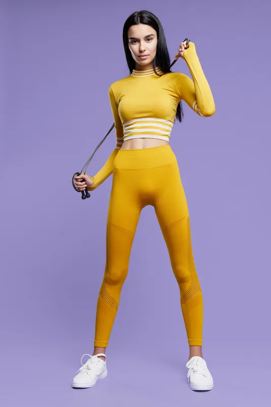 sport fitness woman exercising with jump rope in yellow activewear, standing confidently against purple background, healthy lifestyle and workout concept