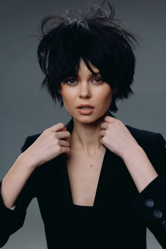 Woman with messy black hair and black blazer looks intensely at camera in studio setting