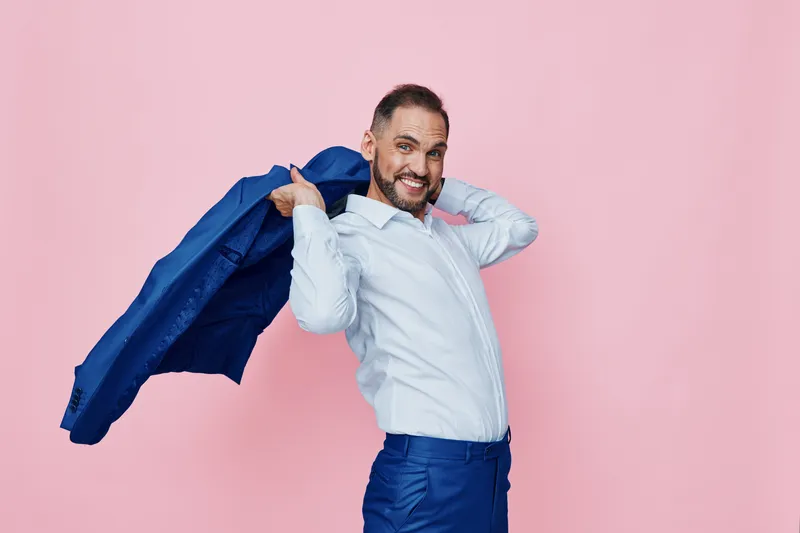 Professional man with a confident pose, isolated on a soft pink background, exuding energy, success, and readiness as he tosses his blazer.