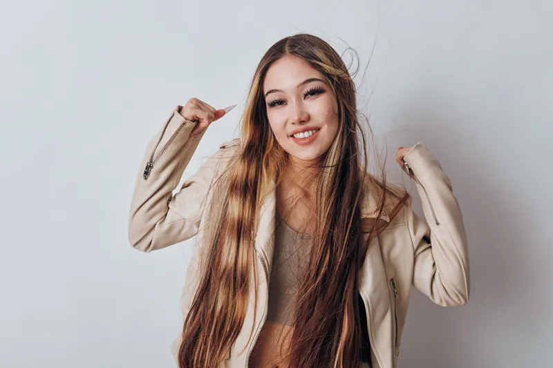 Young woman with long hair smiling wearing beige jacket and casual top in studio with white background for fashion, hairstyle and beauty portrait.