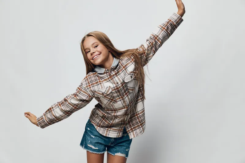 Girl, child, and smiling with long hair wearing plaid shirt and denim shorts. Cheerful kid in joyful pose on plain background for happiness and youth lifestyle.