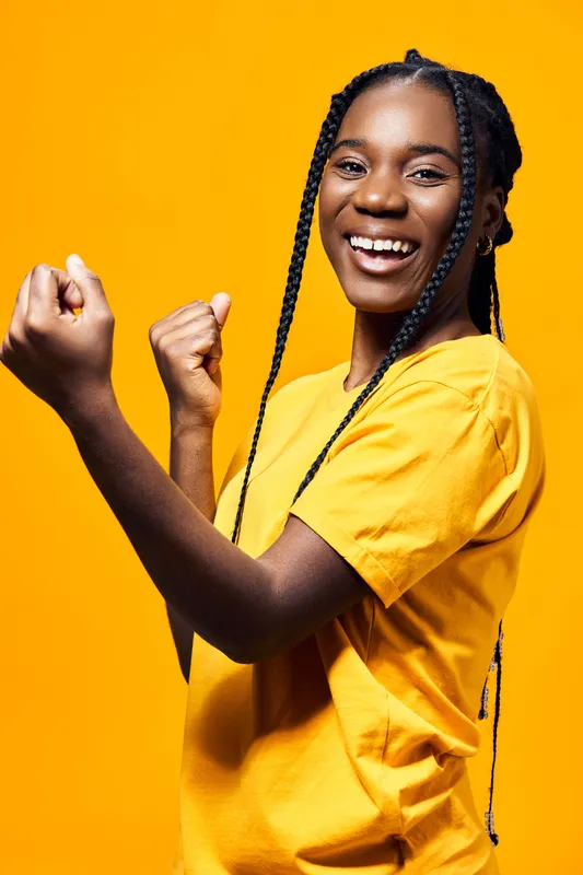 Young Black girl with long braids in a yellow t shirt, expressing joy and positivity against a vibrant yellow background, ideal for health and happiness themes