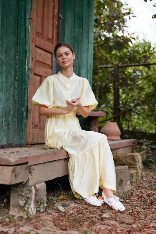 Woman in yellow dress sitting on rustic porch rural portrait, relaxed natural pose with authenticity inclusivity and soft light