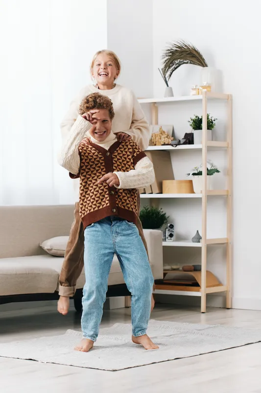 Two children playfully wrestle indoors in a bright living room, a candid moment of laughter and warmth with bare feet, cozy decor, and sunny daylight. Soft furniture and bright decor add warmth.