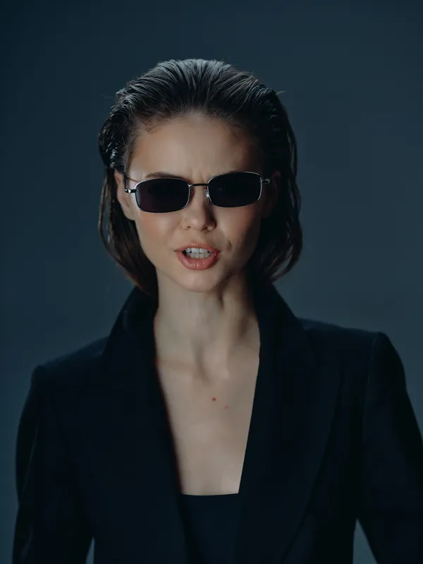Woman wearing stylish sunglasses and black outfit with confident expression in moody studio lighting
