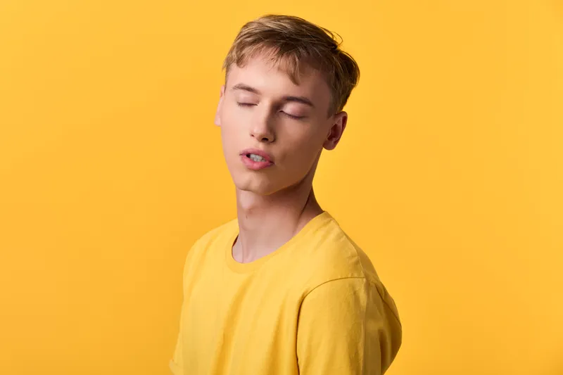 Calm, young male with closed eyes wearing a yellow shirt against a bright yellow backdrop, creating a minimal studio mood ideal for fashion, wellness, or lifestyle campaigns