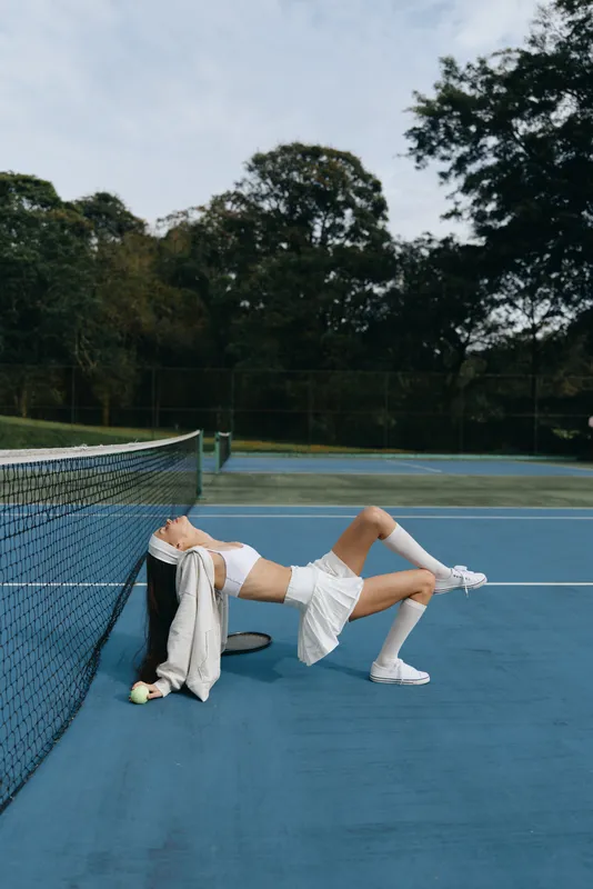 Athletic young woman in sporty outfit relaxing on tennis court, expressing joy and mindfulness with a serene background in soft colors