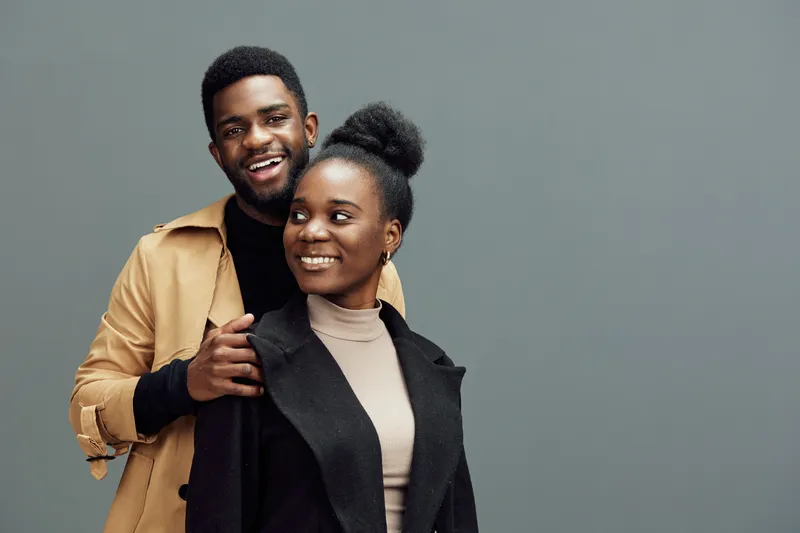 Smiling couple in stylish outfits against a gray background, showcasing modern fashion and joyful emotions, perfect for relationship or lifestyle themes