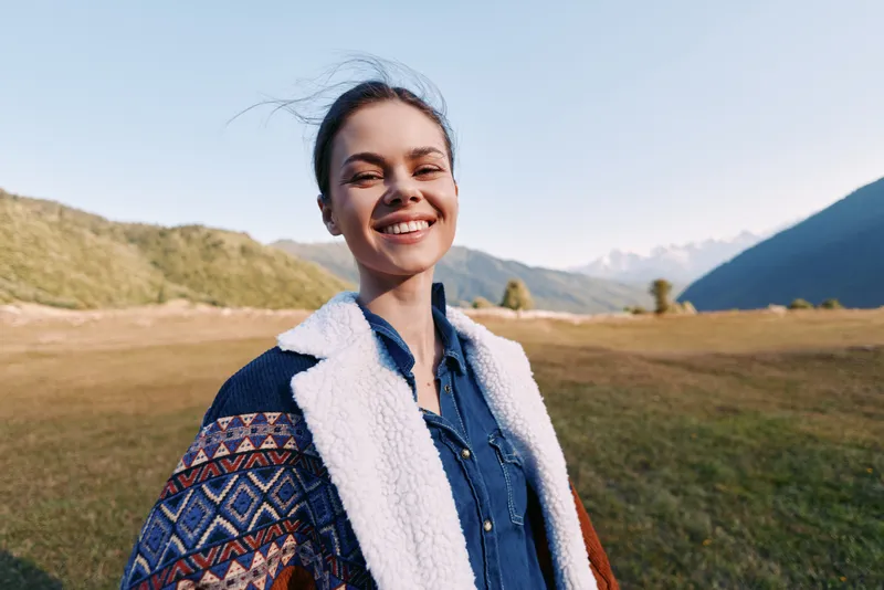 woman smile outdoors mountains meadow jacket portrait nature happy youth enjoying fresh air in scenic landscape, closeup of female traveler in denim shirt and patterned sherpa coat under clear sky