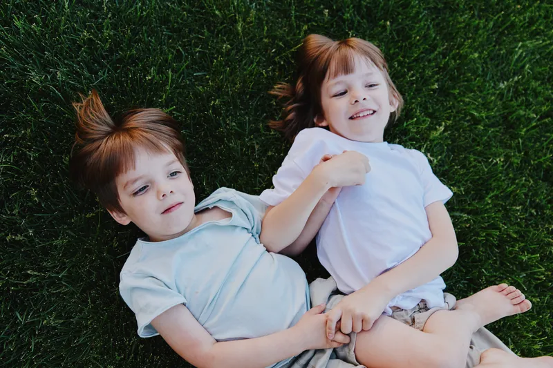 Two happy children playing on green grass, showcasing joy and innocence, with one boy holding the hand of another, smiling brightly together.