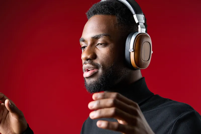 Young Black man enjoying music with headphones on a vibrant red background, showcasing a relaxed and joyful expression, ideal for concepts of music enjoyment and lifestyle