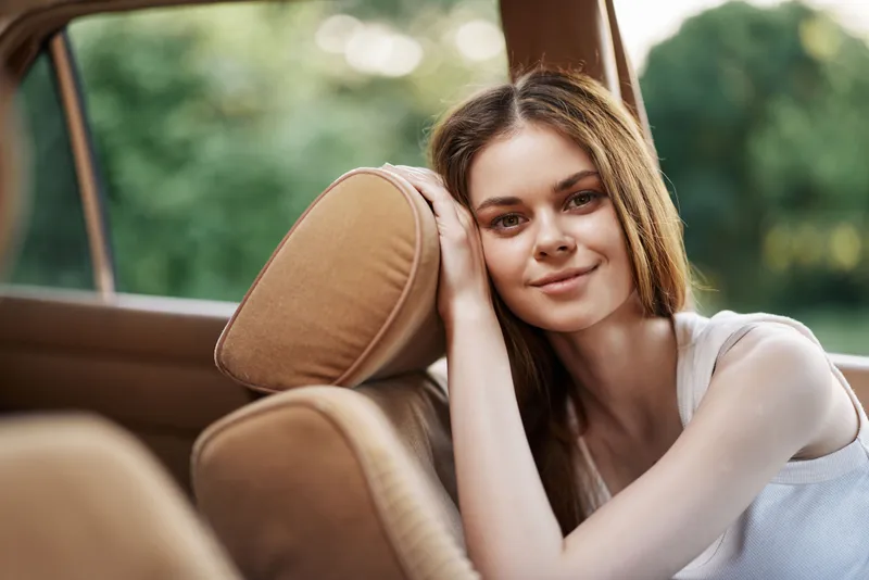 Young woman smiling in a car, with relaxed posture and natural light, reflecting joy and comfort, ideal for lifestyle and travel concepts.