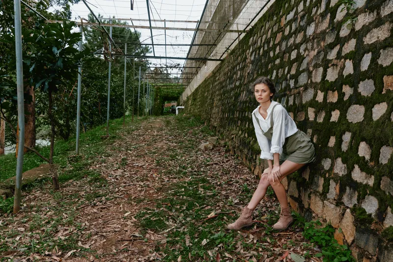 Young woman in nature, wearing casual spring attire with emotions of serenity and contemplation, against a green and earthy background