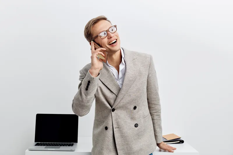 happy young man talking cellphone blockchain technology casual wear standing near laptop digital nomad remote work concept modern workspace