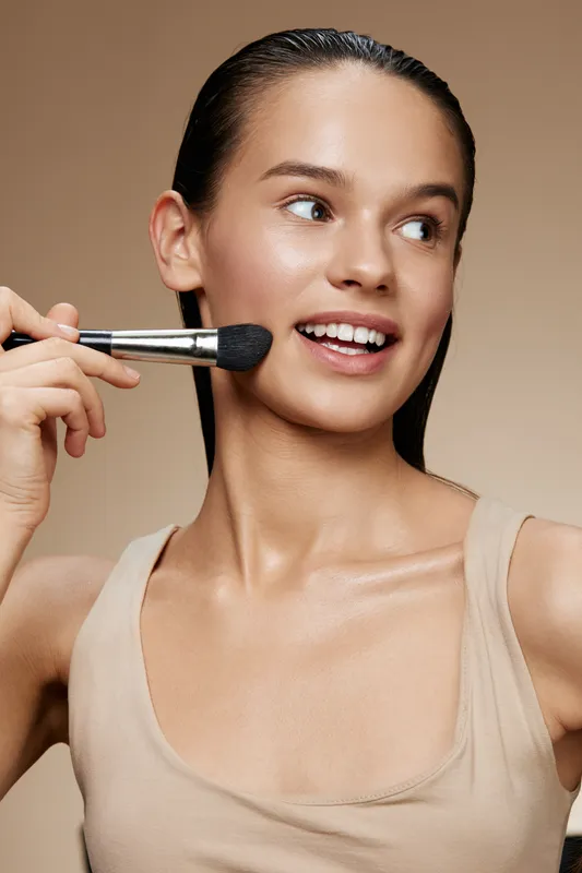 A young model applying makeup with a brush, showcasing healthy skin and a natural look, perfect for beauty and skincare concepts