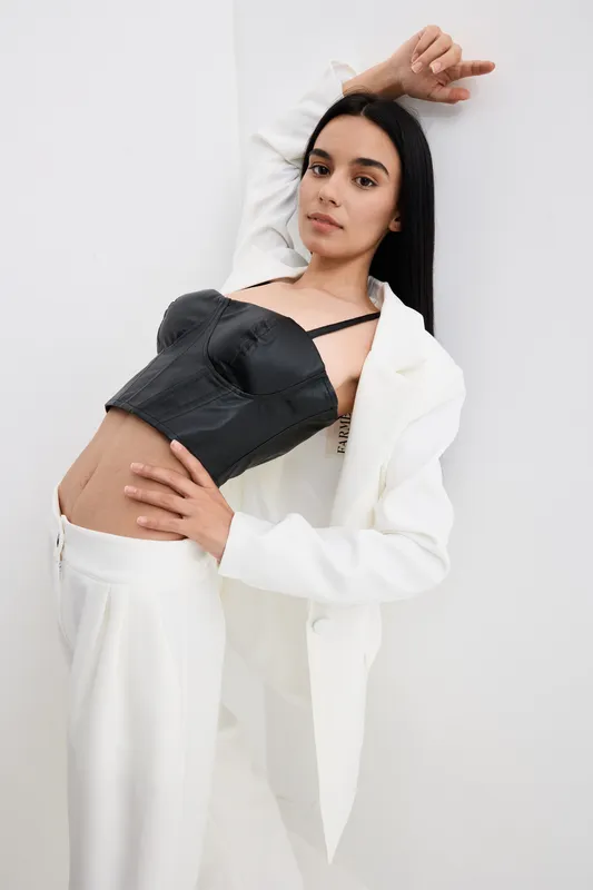 Stylish woman in black corset and white suit posing indoors with a confident expression, minimalistic background, and modern fashion style.