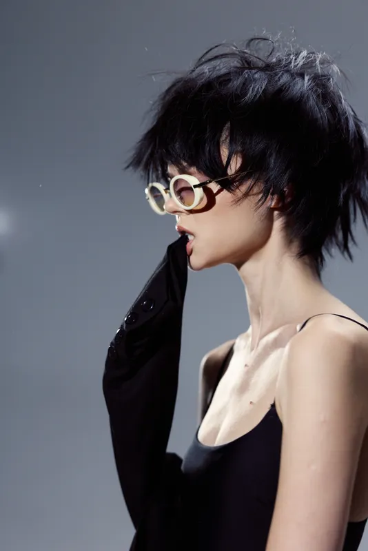 Stylish woman wearing glasses biting black sleeve in moody studio lighting with short hair and pale skin
