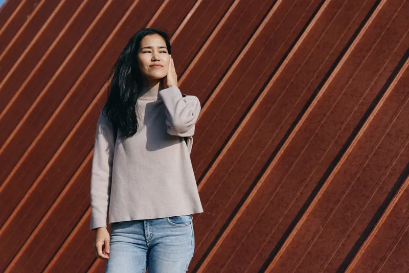 Woman standing in casual sweater and jeans against a diagonal wooden wall, urban style and relaxed mood, outdoor scene focused on streetwear and everyday fashion, natural light