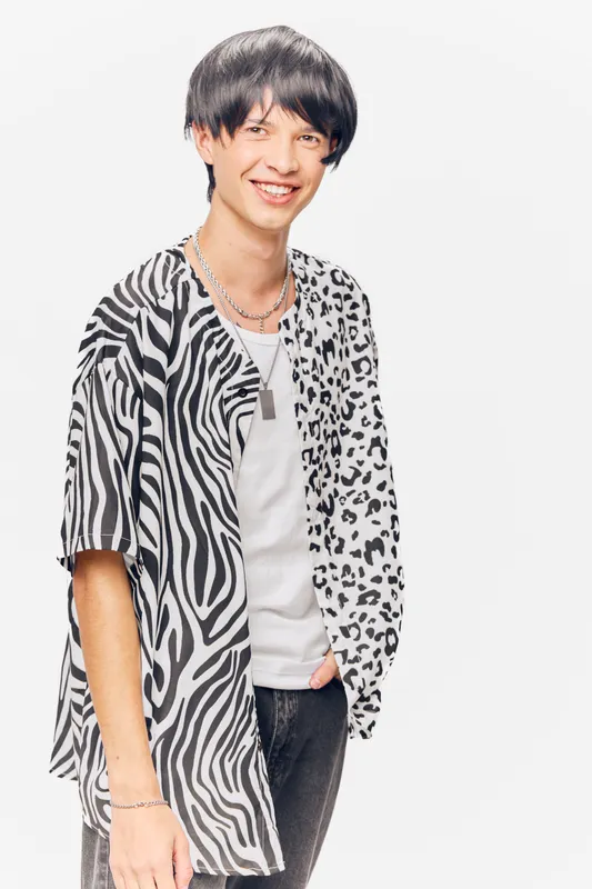 young man smiling wearing a stylish black and white animal print shirt with chains, casual outfit on a white background, cheerful and trendy appearance