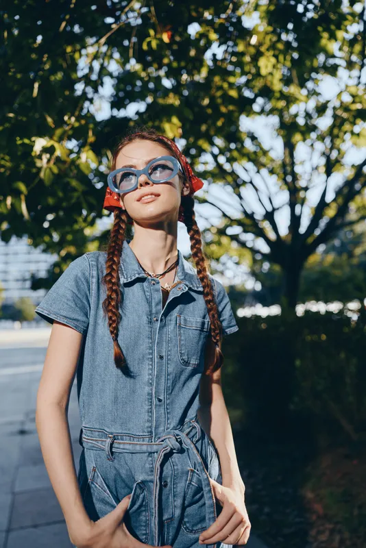 Modern boho-western denim street style woman with braided hair and oversized sunglasses, enjoying sunny outdoor urban lifestyle in film color tones.