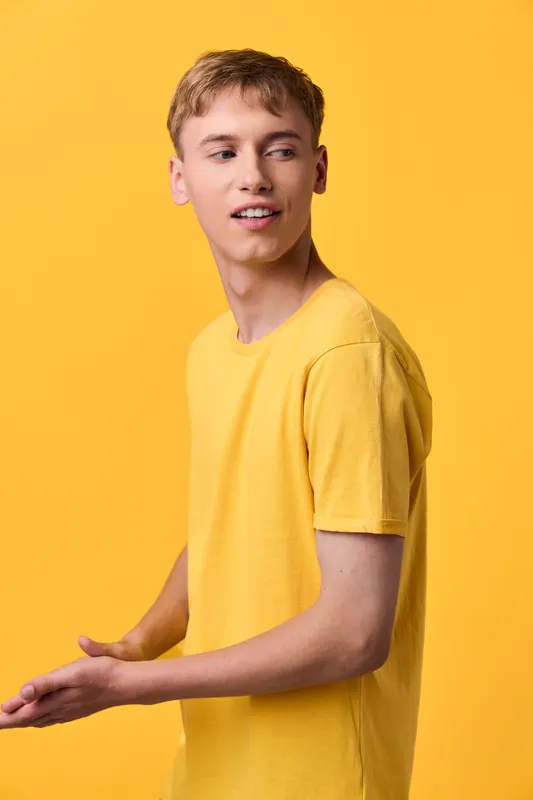 Smiling young man in a bright yellow shirt stands against a vivid yellow backdrop, showcasing casual fashion, relaxed pose, and studio lighting ideal for lifestyle campaigns and fashion catalogs