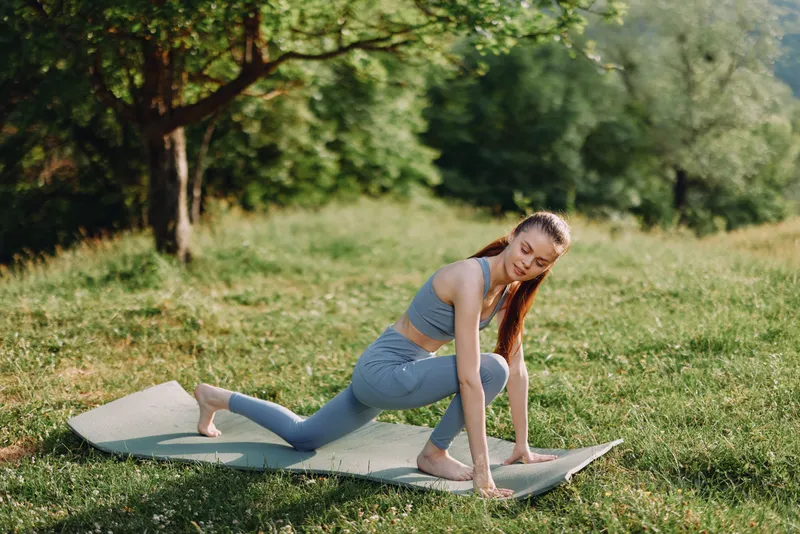 Young woman practicing yoga outdoors in a serene green environment, wearing light blue activewear, exuding calmness and focus, perfect for wellness themes