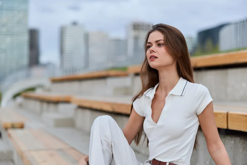 Confident businesswoman sitting outdoors, showcasing a modern, professional look with a stylish outfit amid an urban cityscape.