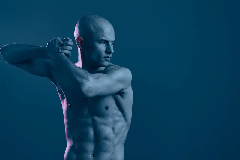 Athletic man stretching in a dynamic pose under cool lighting, conveying strength and focus in a tranquil blue atmosphere, perfect for fitness themes.