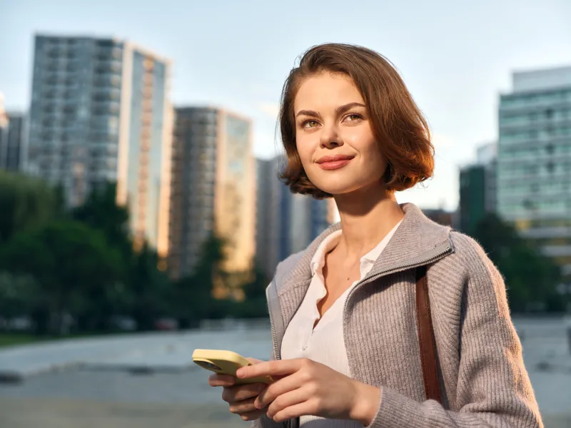 A cheerful professional woman is seen texting in a modern urban setting. She smiles and appears engaged, creating a positive and dynamic atmosphere as she moves through a contemporary cityscape.