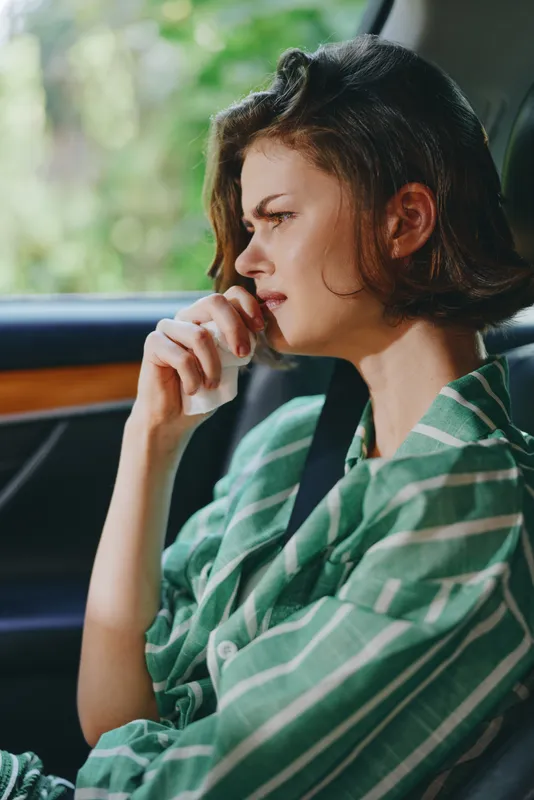 Profile shot of a woman seated in a car, thoughtful expression, hand near her mouth, soft natural light, wearing a green striped shirt.