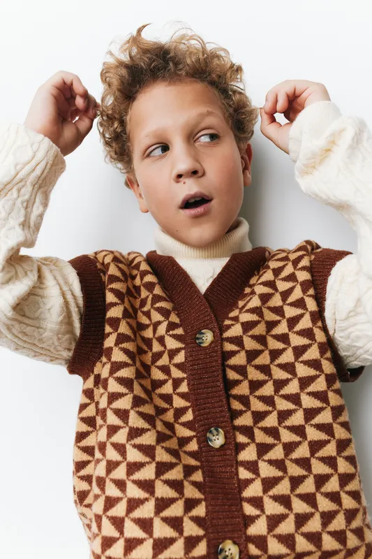 Authentic candid portrait of a student wearing a geometric knitted vest, capturing a spontaneous moment, curiosity and playful innocence during school life.