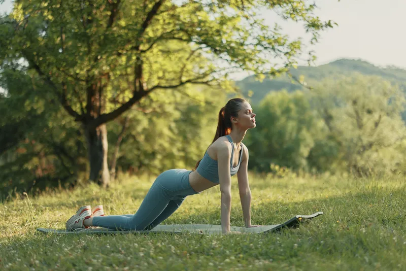 Young woman in athletic wear practicing yoga in a natural setting, showcasing flexibility, tranquility, and health The serene background enhances the concept of wellness