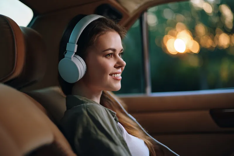 Young woman with headphones enjoying music in a car, capturing a moment of joy and relaxation during sunset. Perfect for themes of leisure and music appreciation.